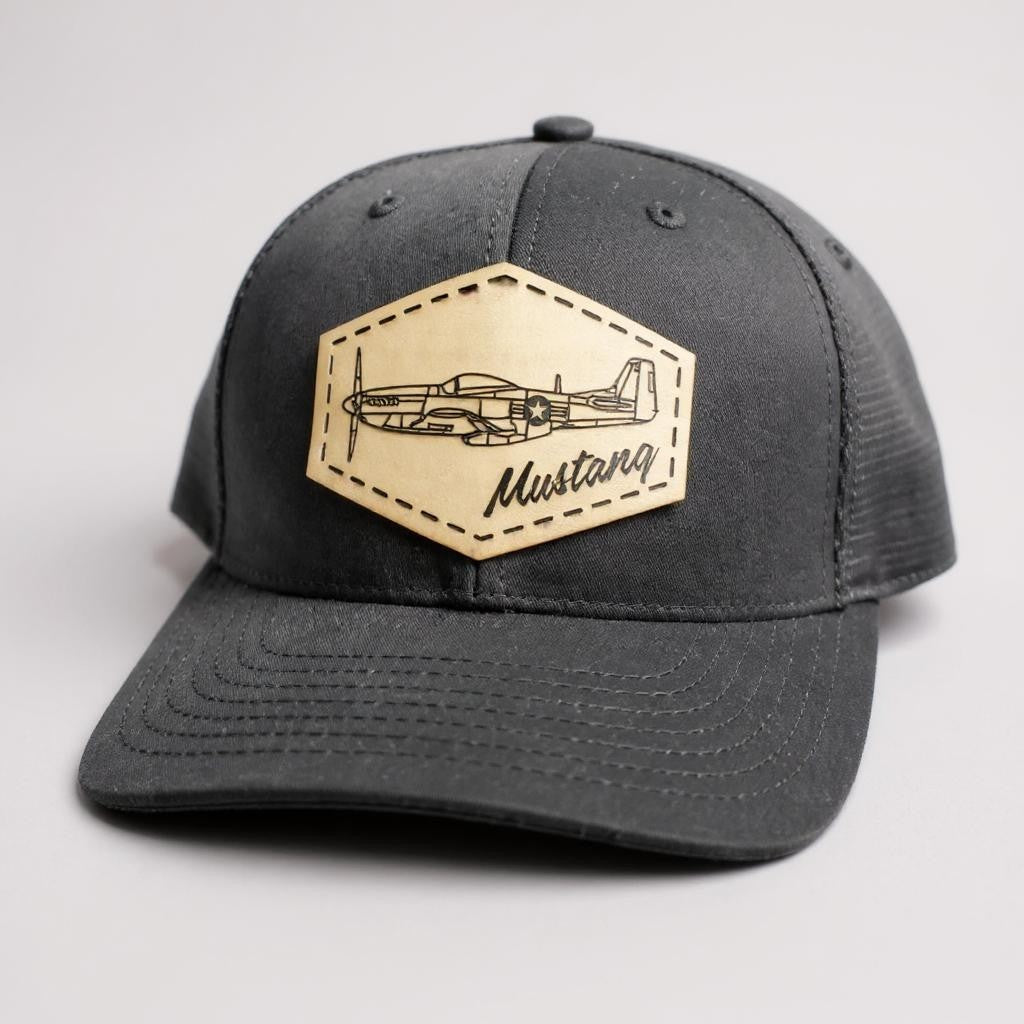 Gray and black trucker hat with a beige patch featuring an airplane and 'Mustang' text on a white background.
