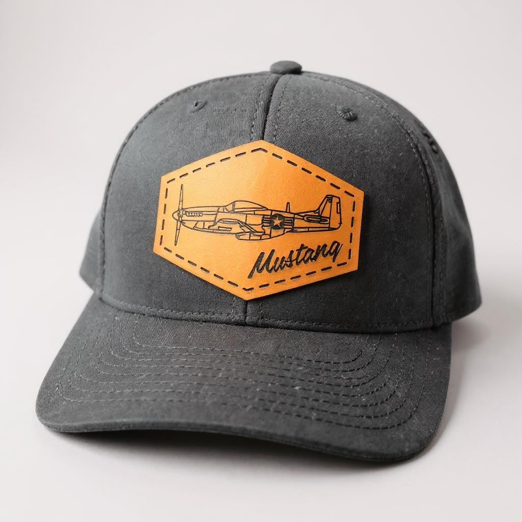 Black hat with brown leather patch featuring an airplane design on a light gray background