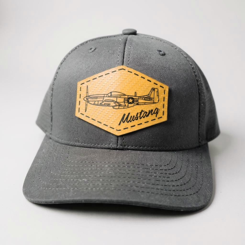 Black trucker hat with a gold patch featuring an airplane and 'Mustang' text on a white background.