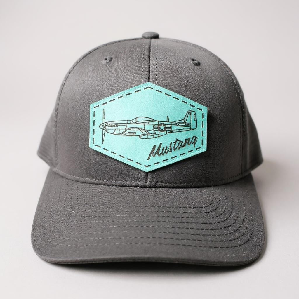 Gray and black trucker hat with a teal patch featuring an airplane and 'Mustang' text on a white background.