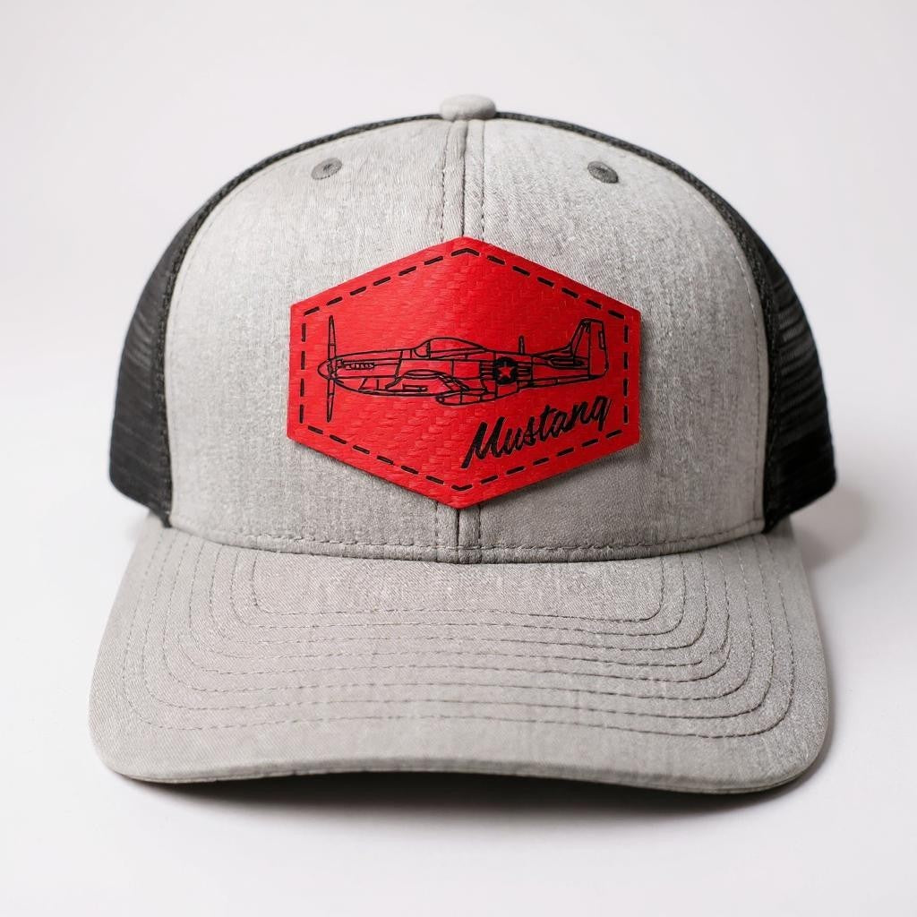 Gray and black trucker hat with a red textured patch featuring an airplane and 'Mustang' text on a white background.
