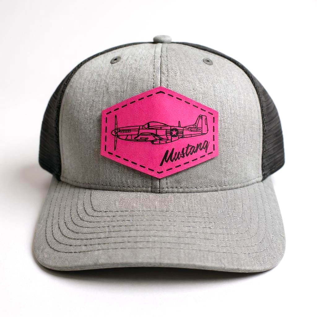 Gray and black trucker hat with a pink patch featuring an airplane and 'Mustang' text on a white background.