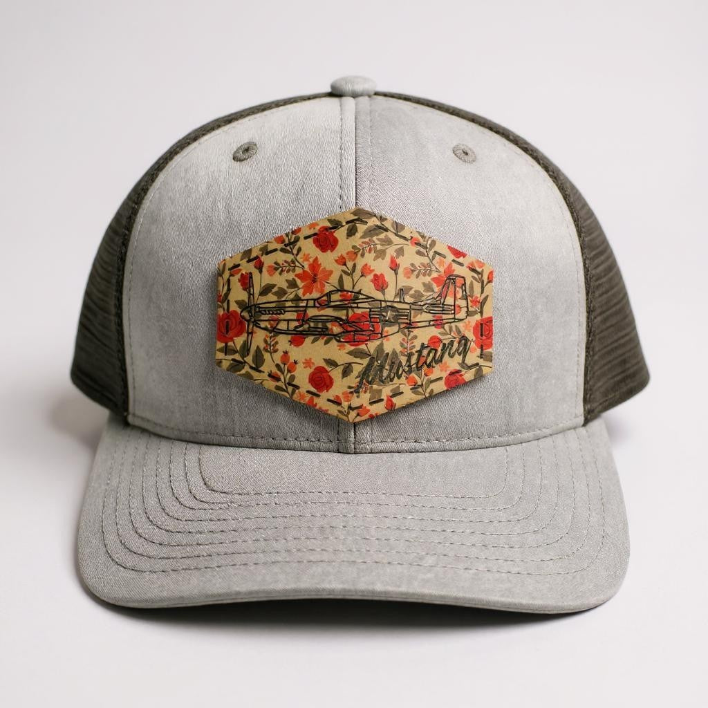 Gray and black trucker hat with floral patch and 'Mustang' airplane on a white background