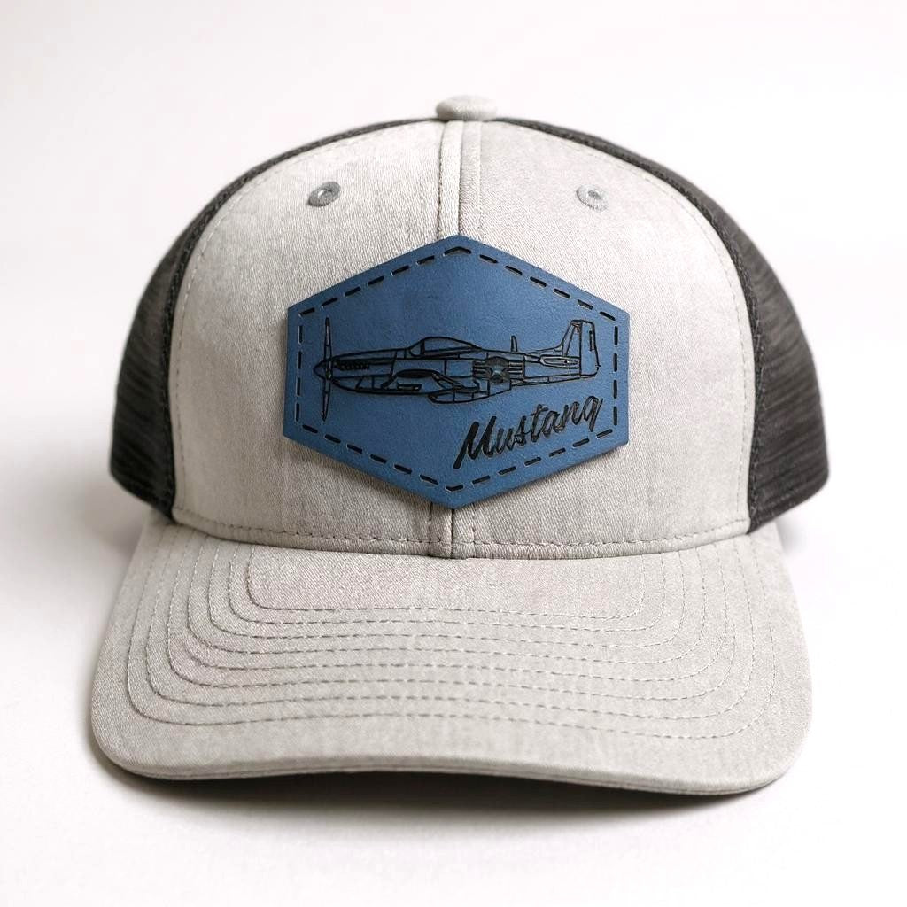 Gray and black trucker hat with a blue patch featuring an airplane and 'Mustang' text on a white background.