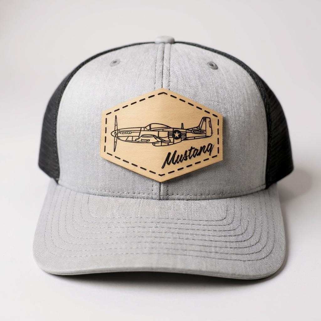 Gray and black trucker hat with a beige patch featuring an airplane and 'Mustang' text on a white background.