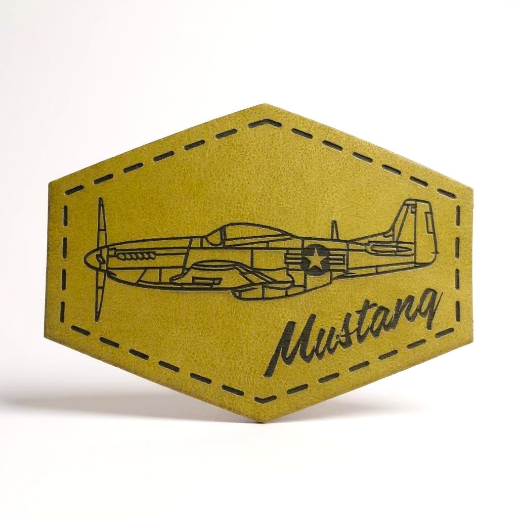 Hexagonal green leather patch with a black outline of an airplane and 'Mustang' text on a white background
