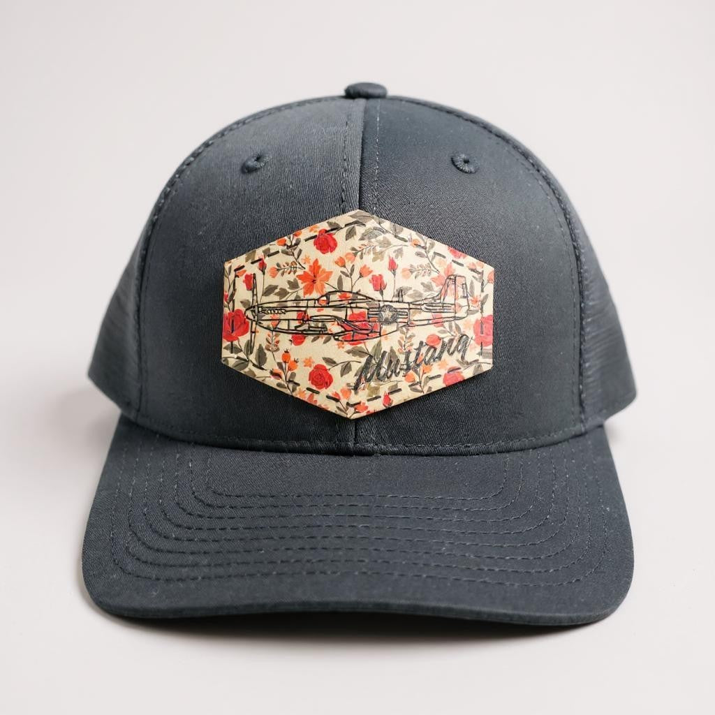 Black Trucker hat with a floral patch featuring the word 'Mustang' and the airplane on a light gray background