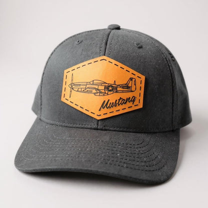 Black hat with brown leather patch featuring an airplane design on a light gray background
