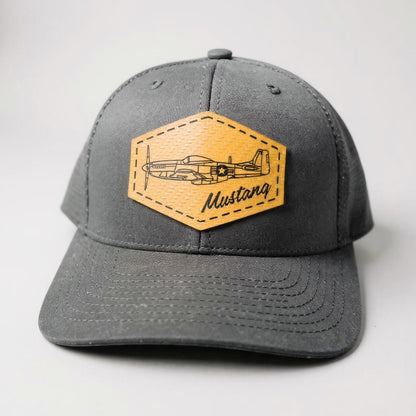 Black trucker hat with a gold patch featuring an airplane and 'Mustang' text on a white background.