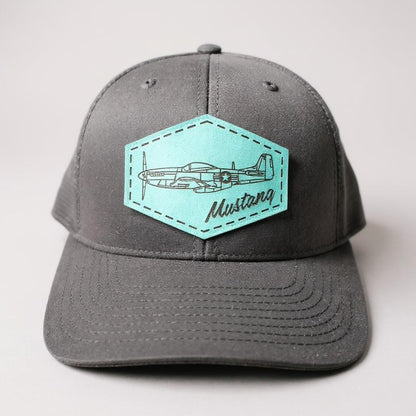 Gray and black trucker hat with a teal patch featuring an airplane and 'Mustang' text on a white background.