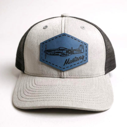 Gray and black trucker hat with a blue patch featuring an airplane and 'Mustang' text on a white background.