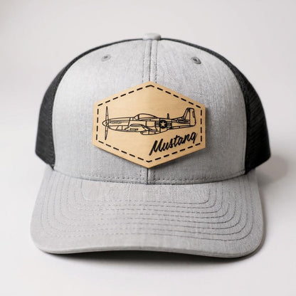 Gray and black trucker hat with a beige patch featuring an airplane and 'Mustang' text on a white background.