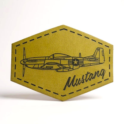 Hexagonal green leather patch with a black outline of an airplane and 'Mustang' text on a white background